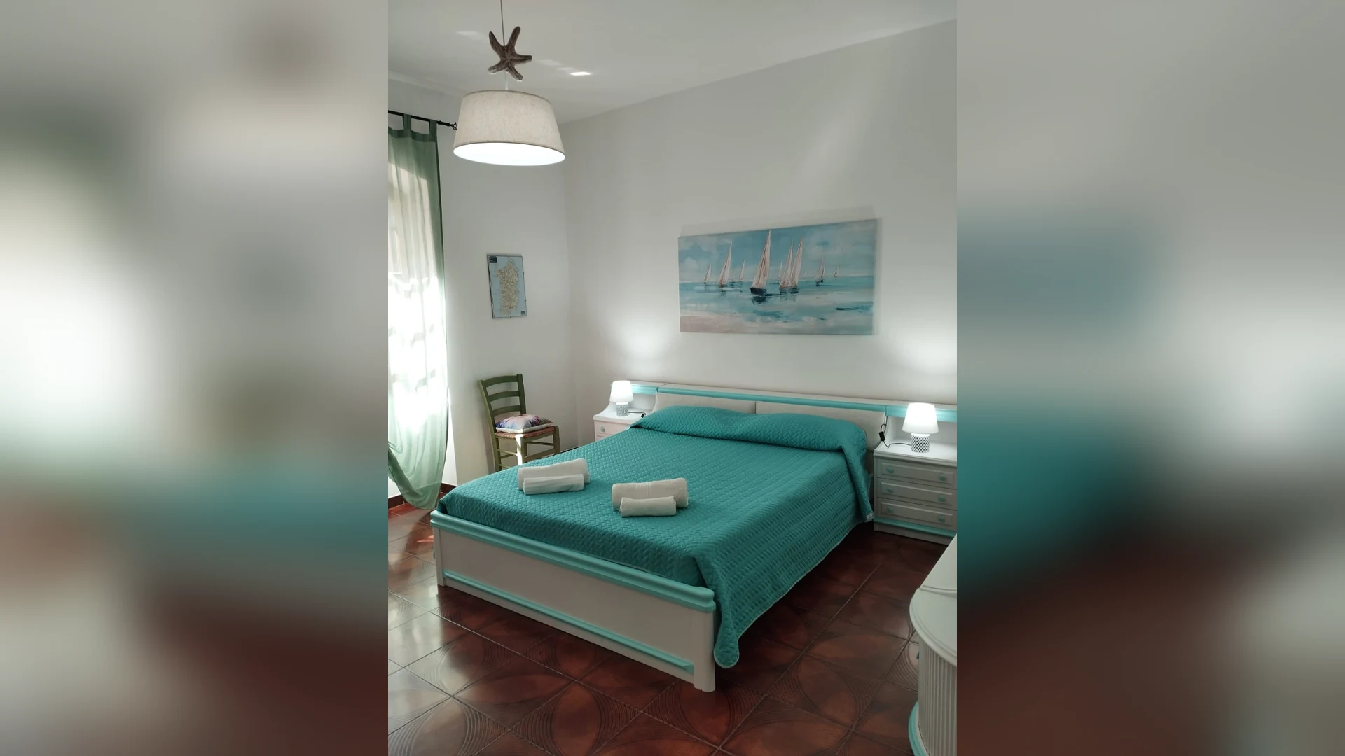 La camera matrimoniale con il copriletto turchese e il quadro delle barche a vela