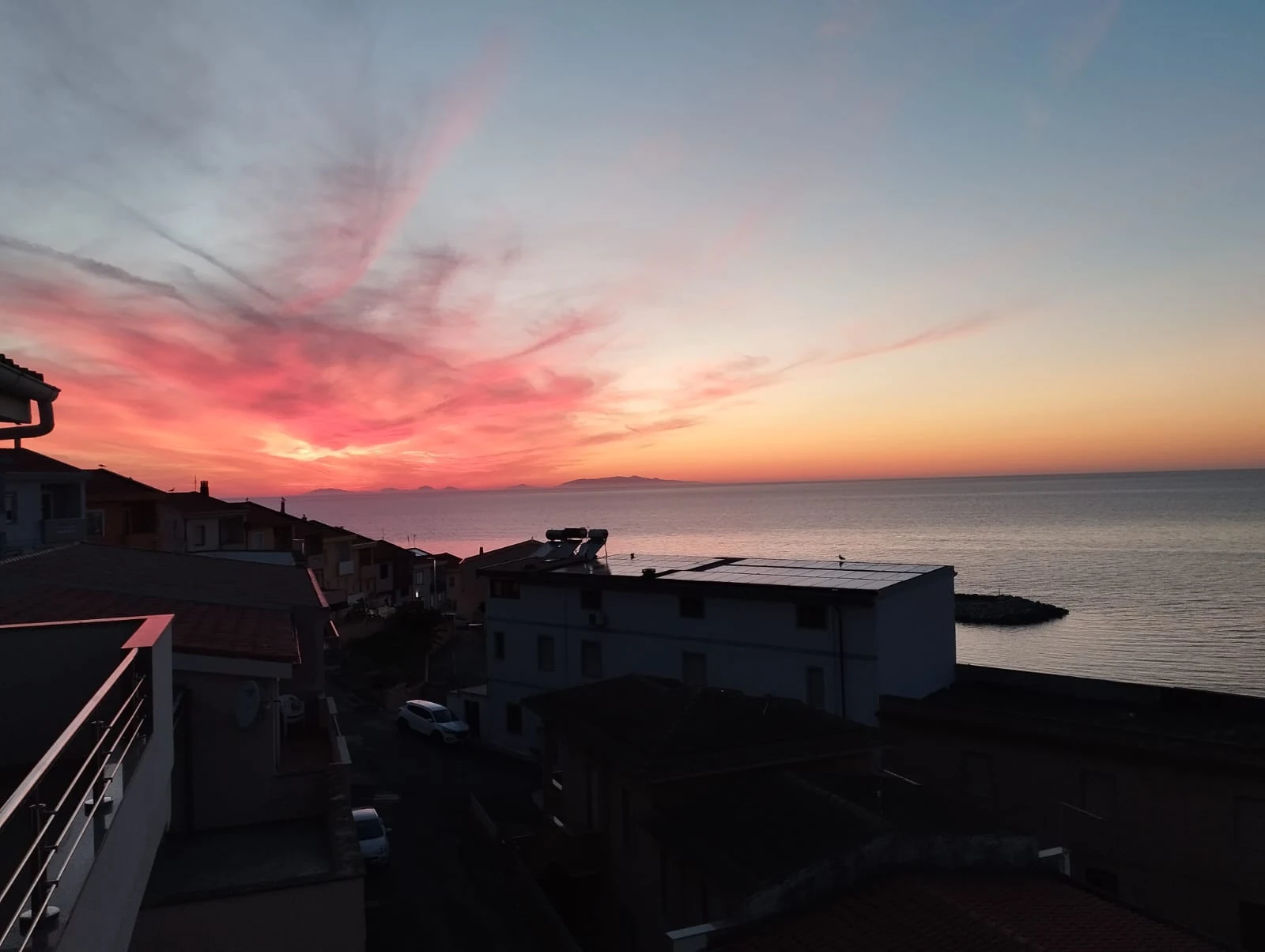 Il cielo rosa del tramonto sopra i tetti e il golfo dell'Asinara
