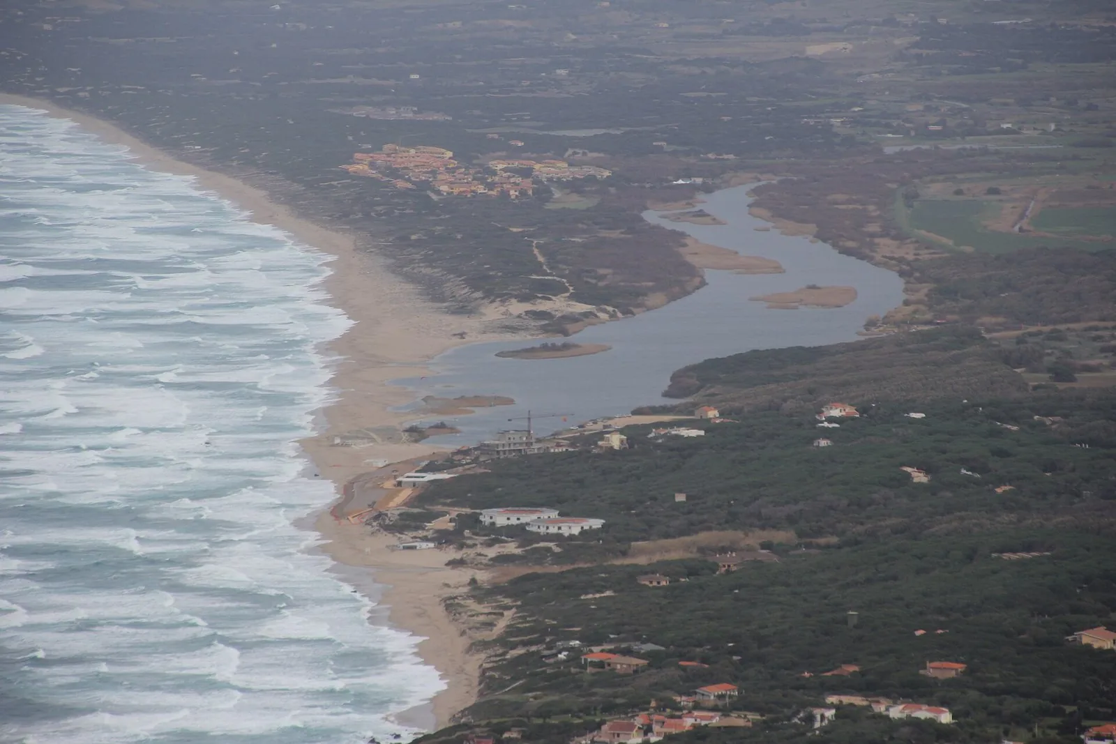 Spiaggia di sabbia chiara a Lu Bagnu, Castelsardo, con mare calmo e il promontorio del borgo in lontananza